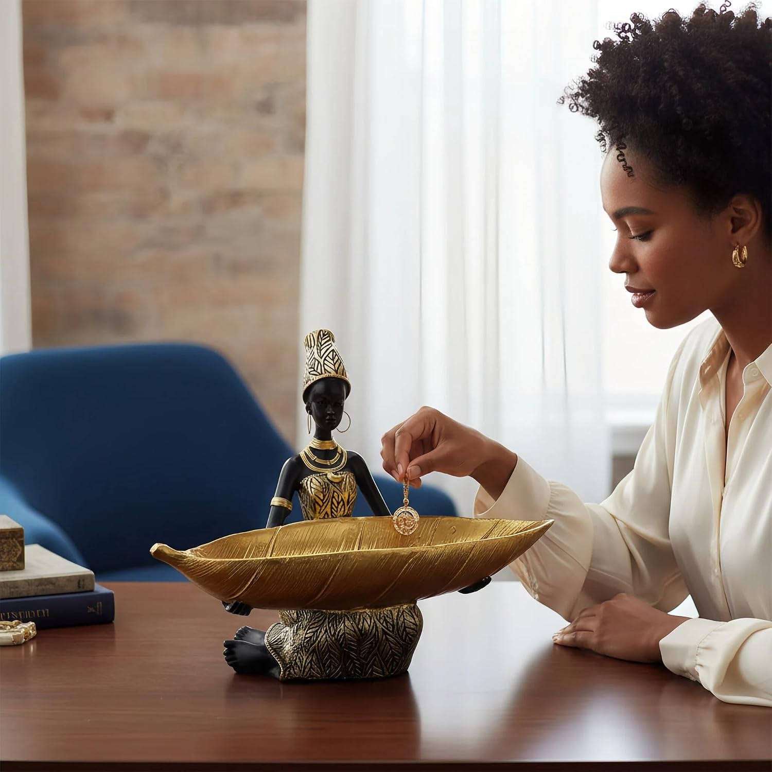 Person placing a pendant into a large gold bowl held by a seated black-and-gold figurine on a wood table.
