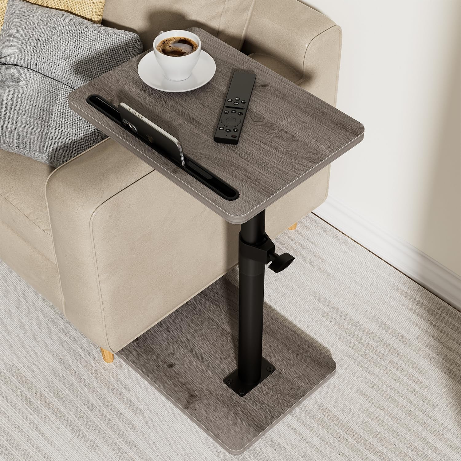 Close angled view showing gray wood tabletop with built-in slot holding a phone, cup and remote on top.