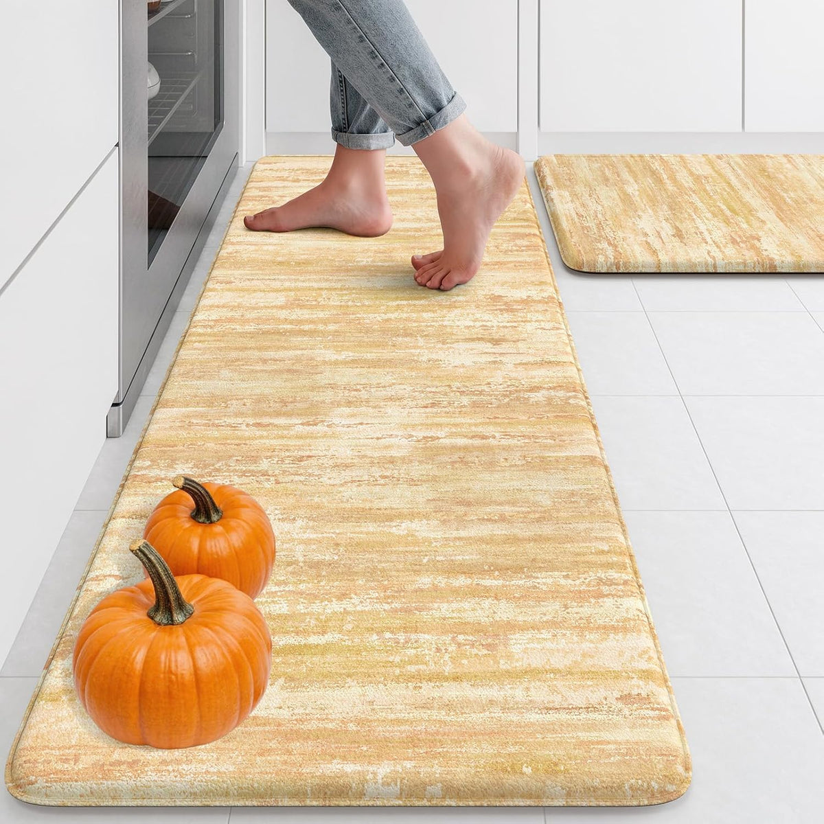 Golden-yellow cushioned runner with two small pumpkins on one end and a person standing on the mat near an oven.