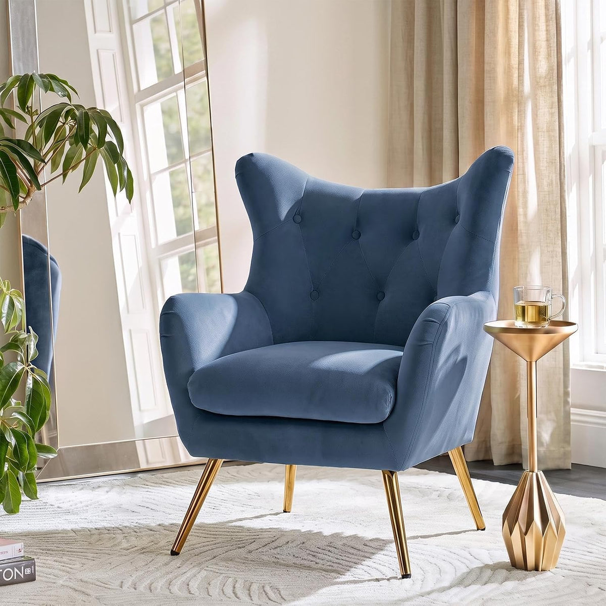 Slate blue velvet wingback chair shown in soft window light highlighting tufted back and angled gold legs.