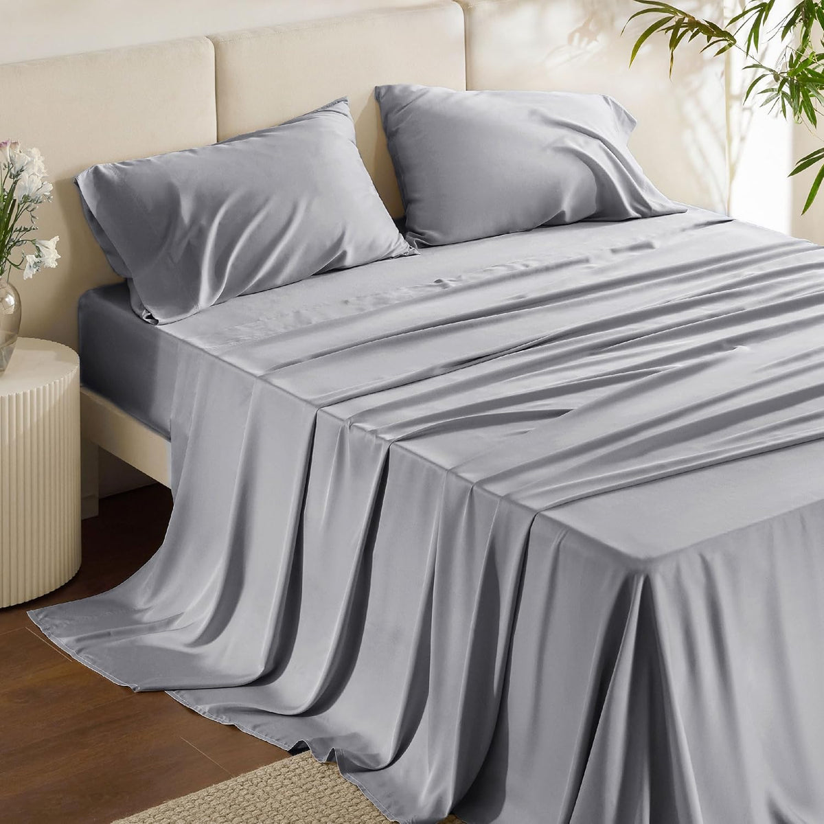 Close-up of a bed showing two gray pillowcases and smooth gray sheets cascading over the side to the floor.