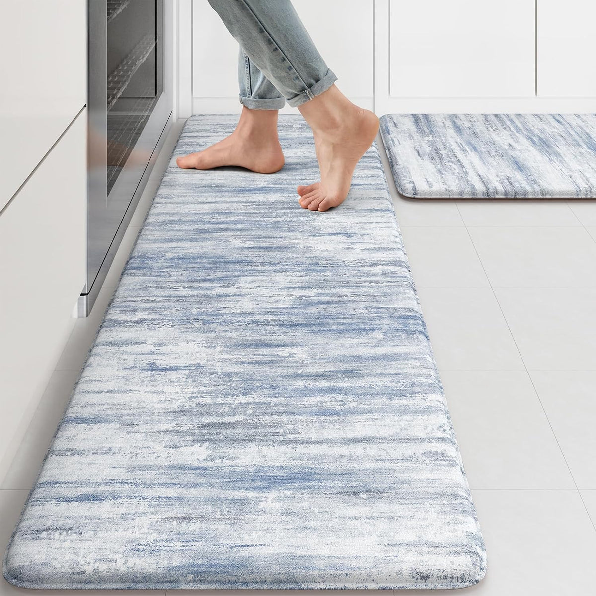 Angled view of a blue-and-white abstract kitchen mat with bare feet stepping on it.