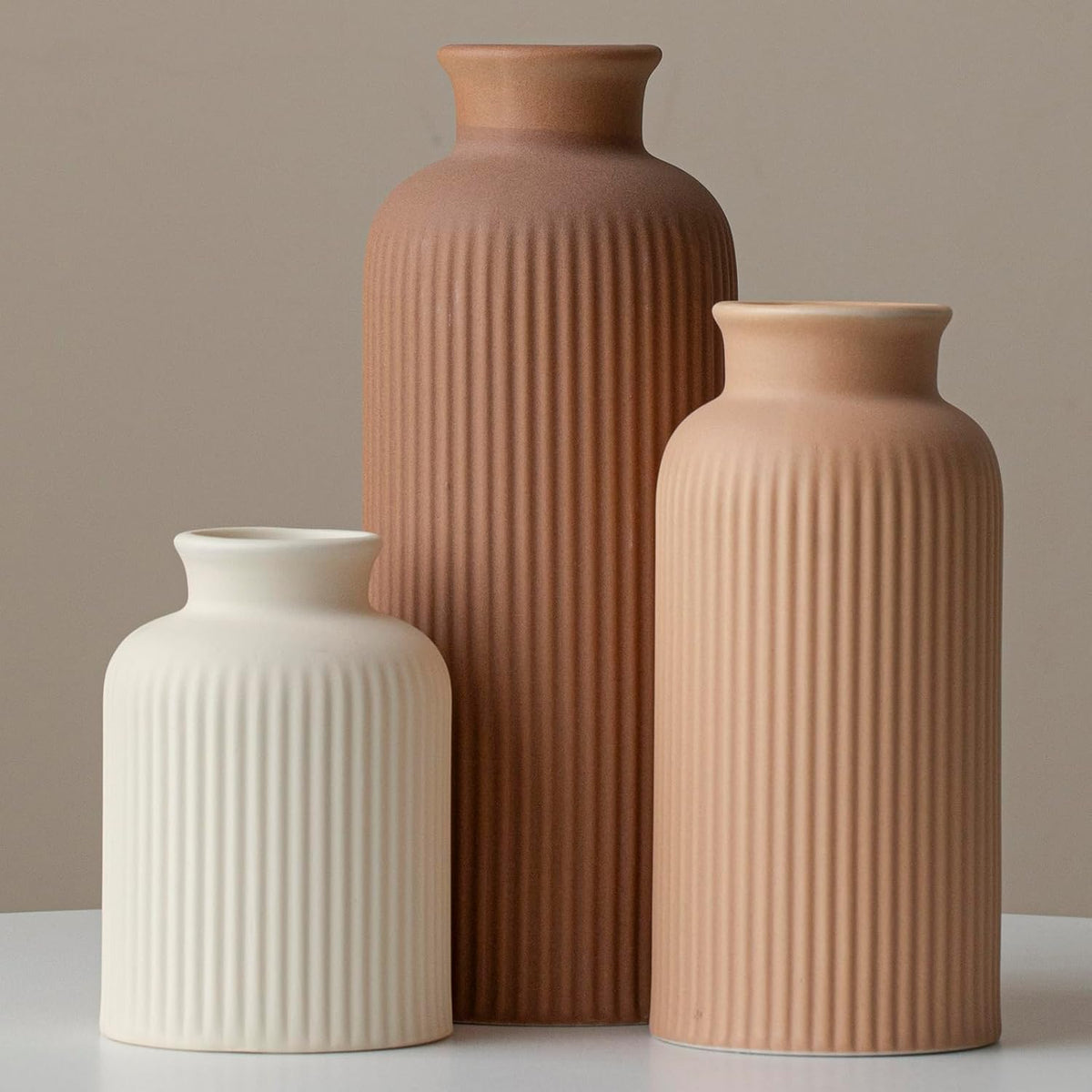 Three ceramic 3-piece ribbed vases in cream white, light terracotta and rich brown, front view on a table.