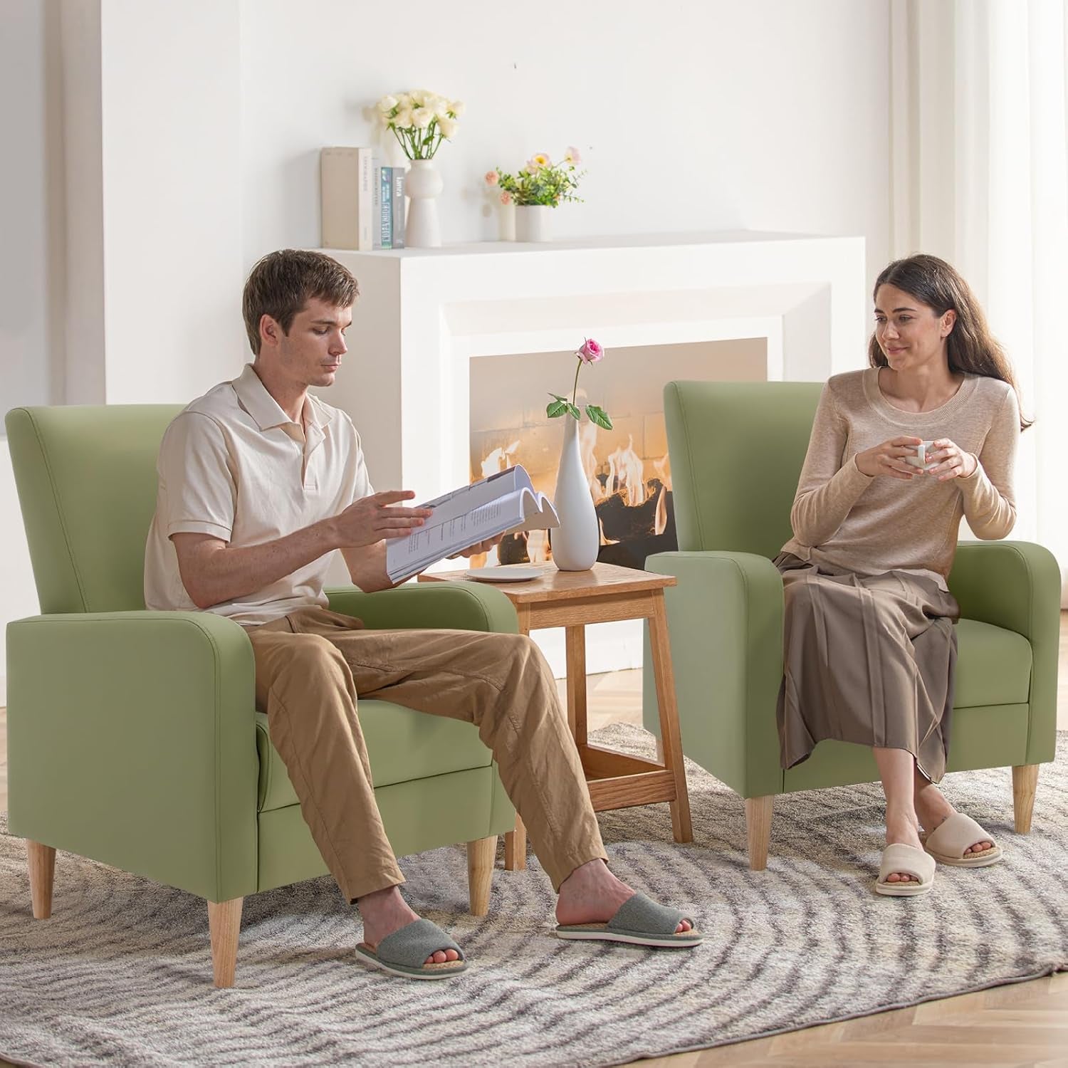 Two green high-back accent chairs with wooden legs flanking a small table in a bright room, people seated.
