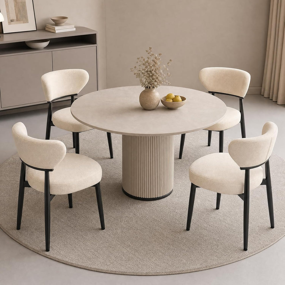 Four beige upholstered dining chairs with curved backs and black legs around a round table.