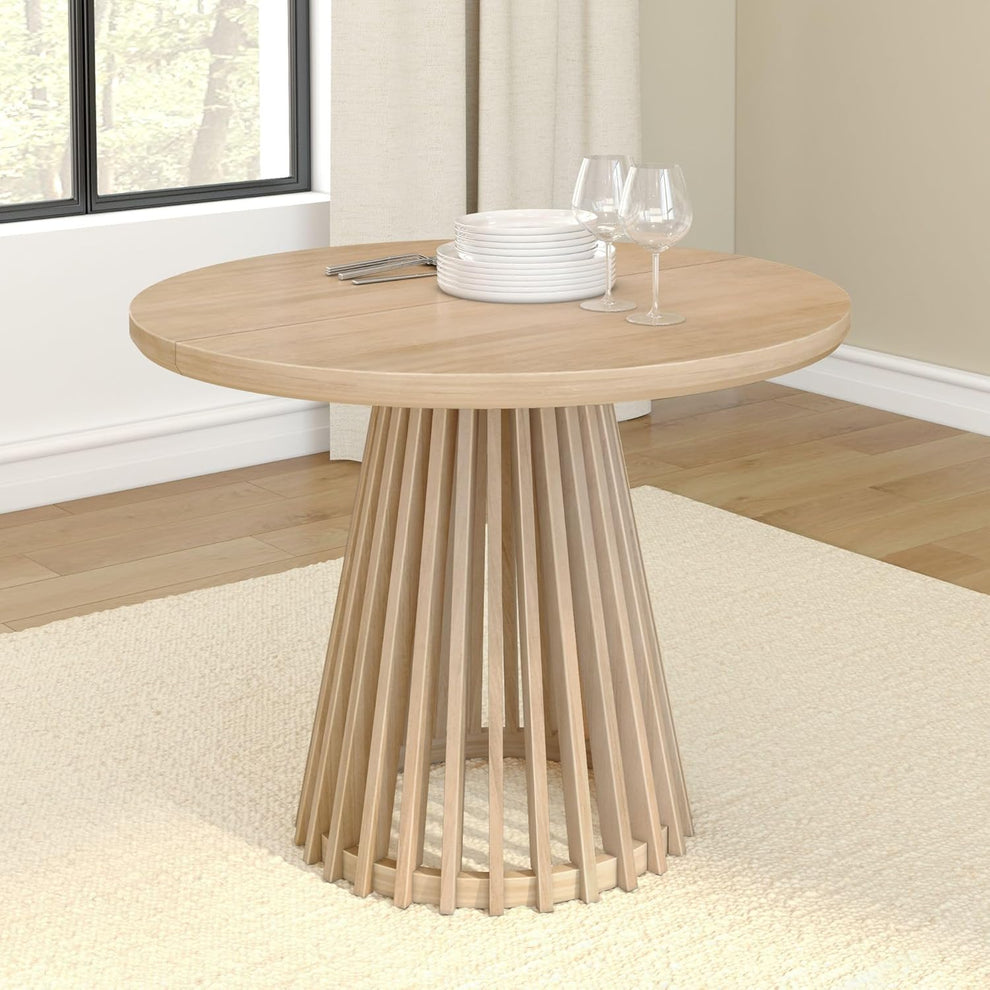 Round dining table in blonde finish showing full tabletop and slatted pedestal base from front-left angle