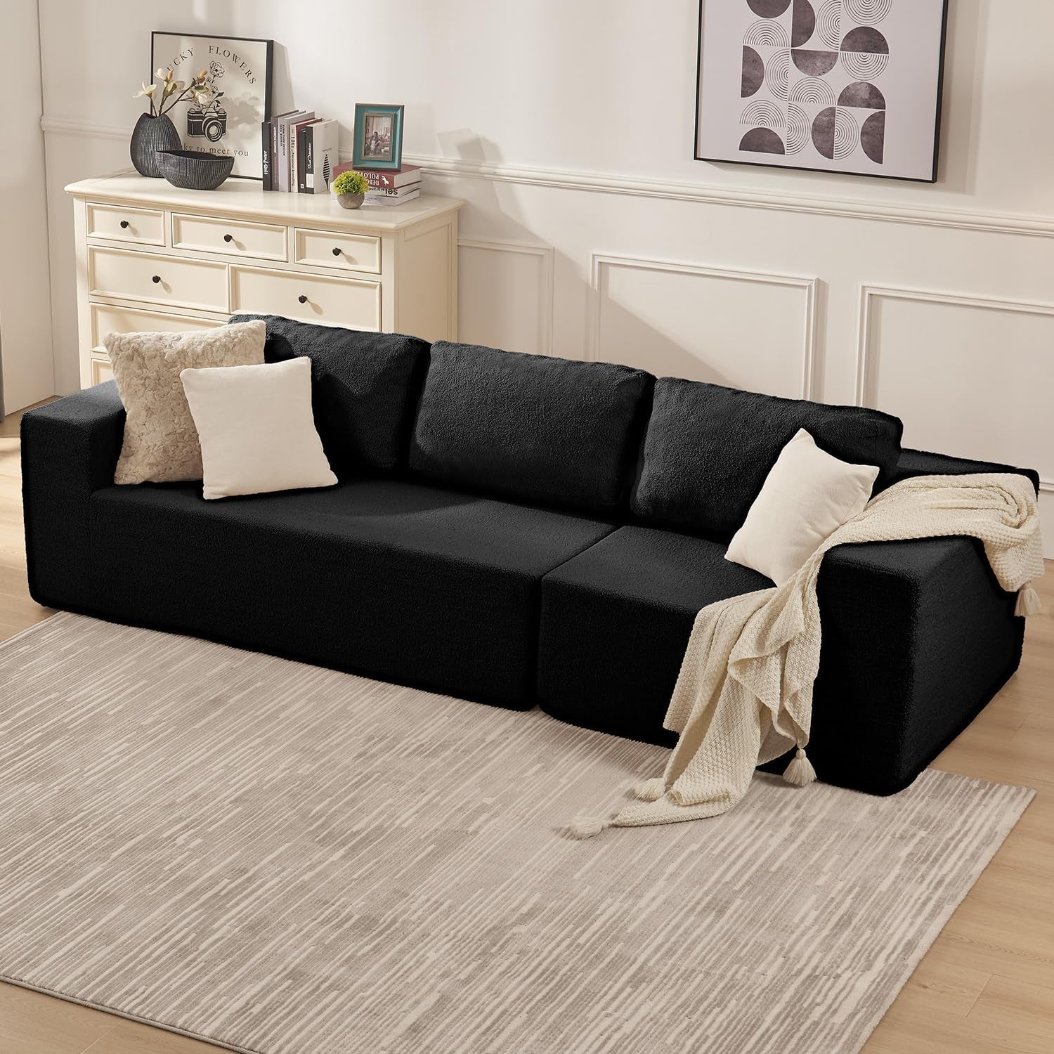 Low-angle view of a black L-shaped modular sofa with throw pillows and a cream blanket in a living room.