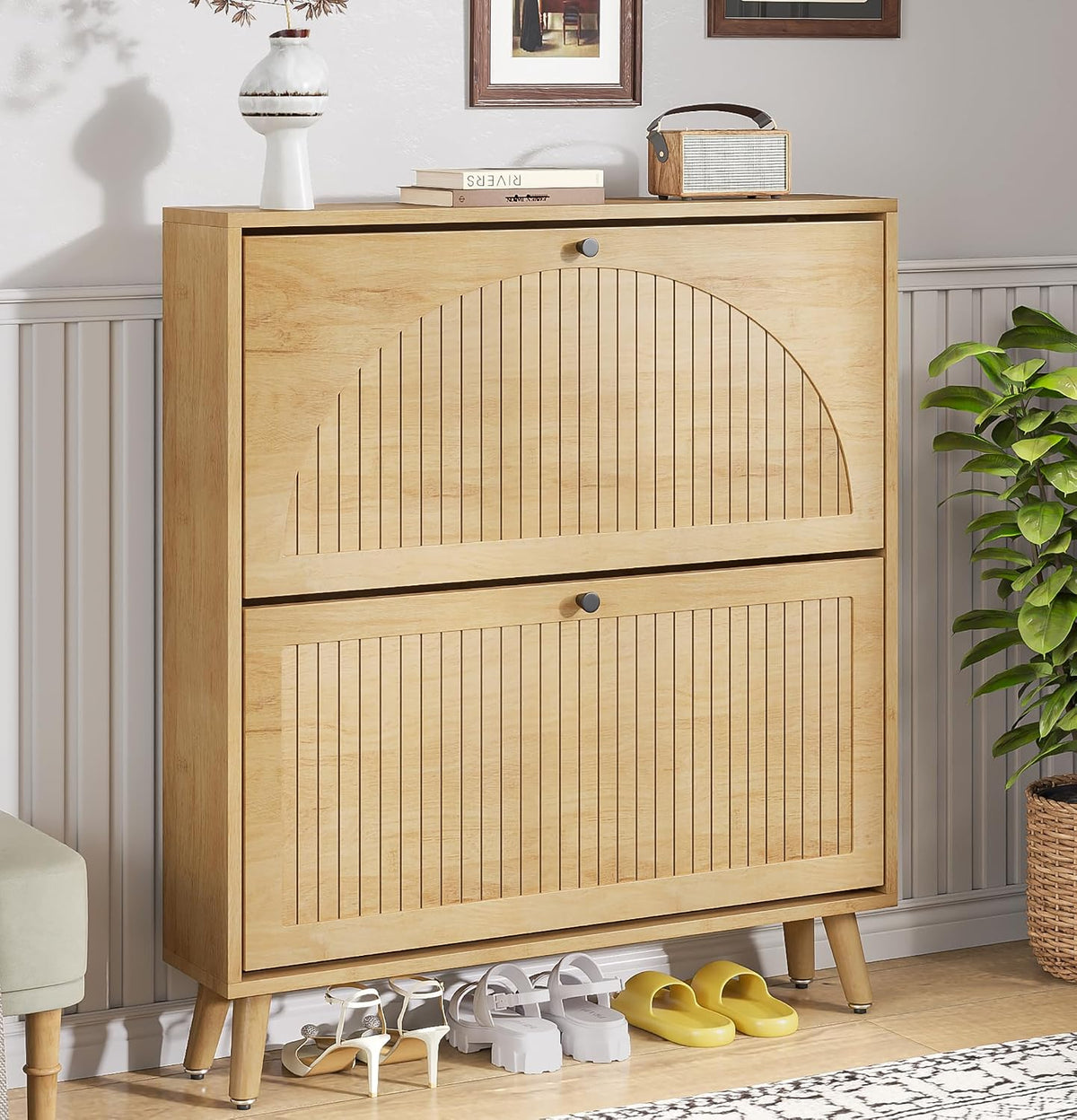 Natural-finish two-drawer shoe cabinet with semicircle fluted fronts, round knobs, tapered legs and shoes tucked beneath.