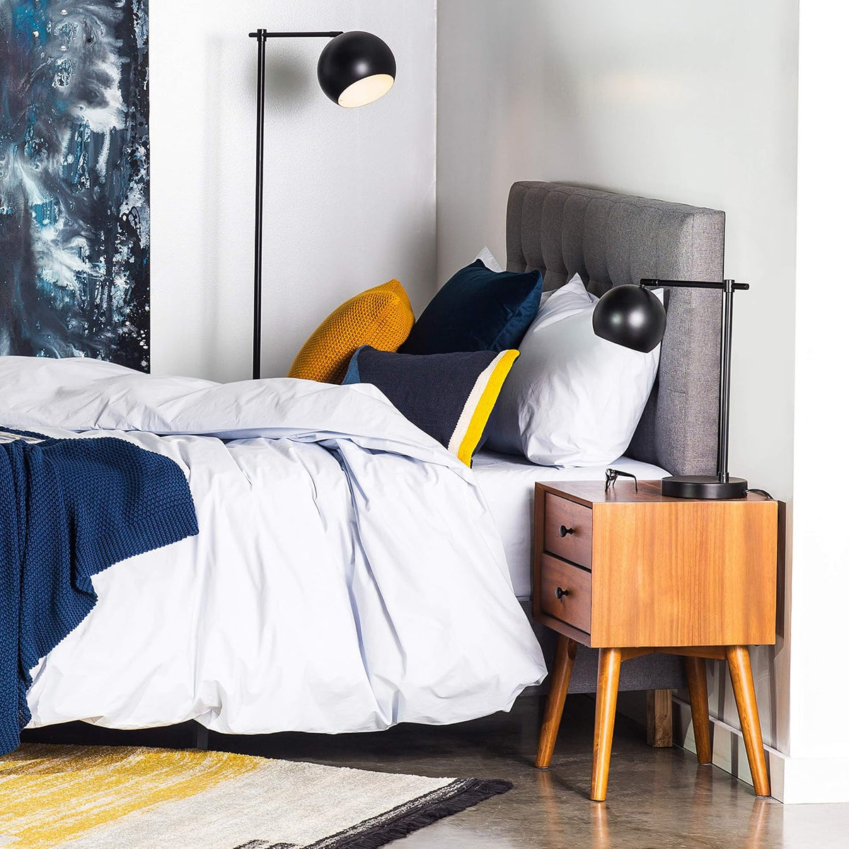 Mid-century two-drawer nightstand in warm wood placed beside a bed with lamp and grey headboard