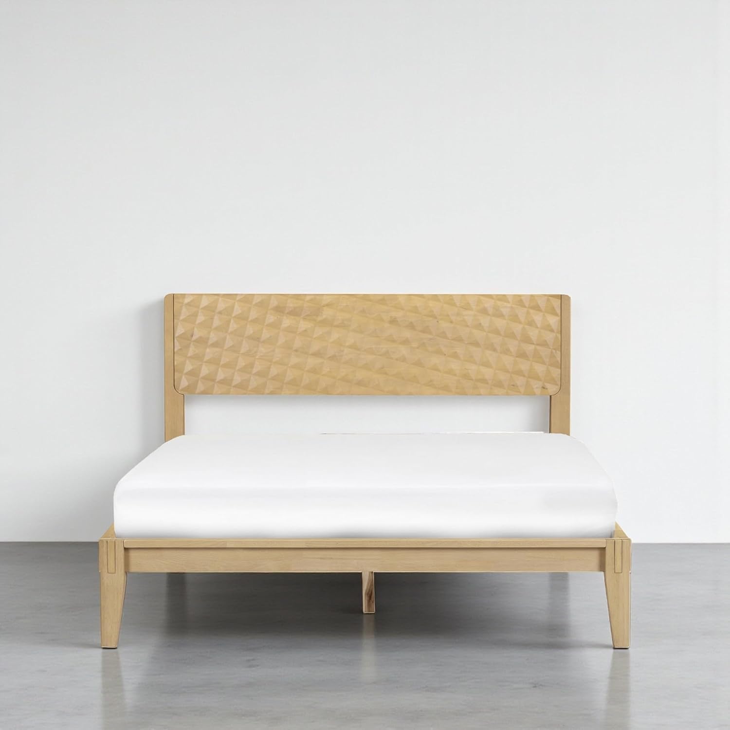 Front view of a queen bed in a light natural wood finish with carved geometric headboard.