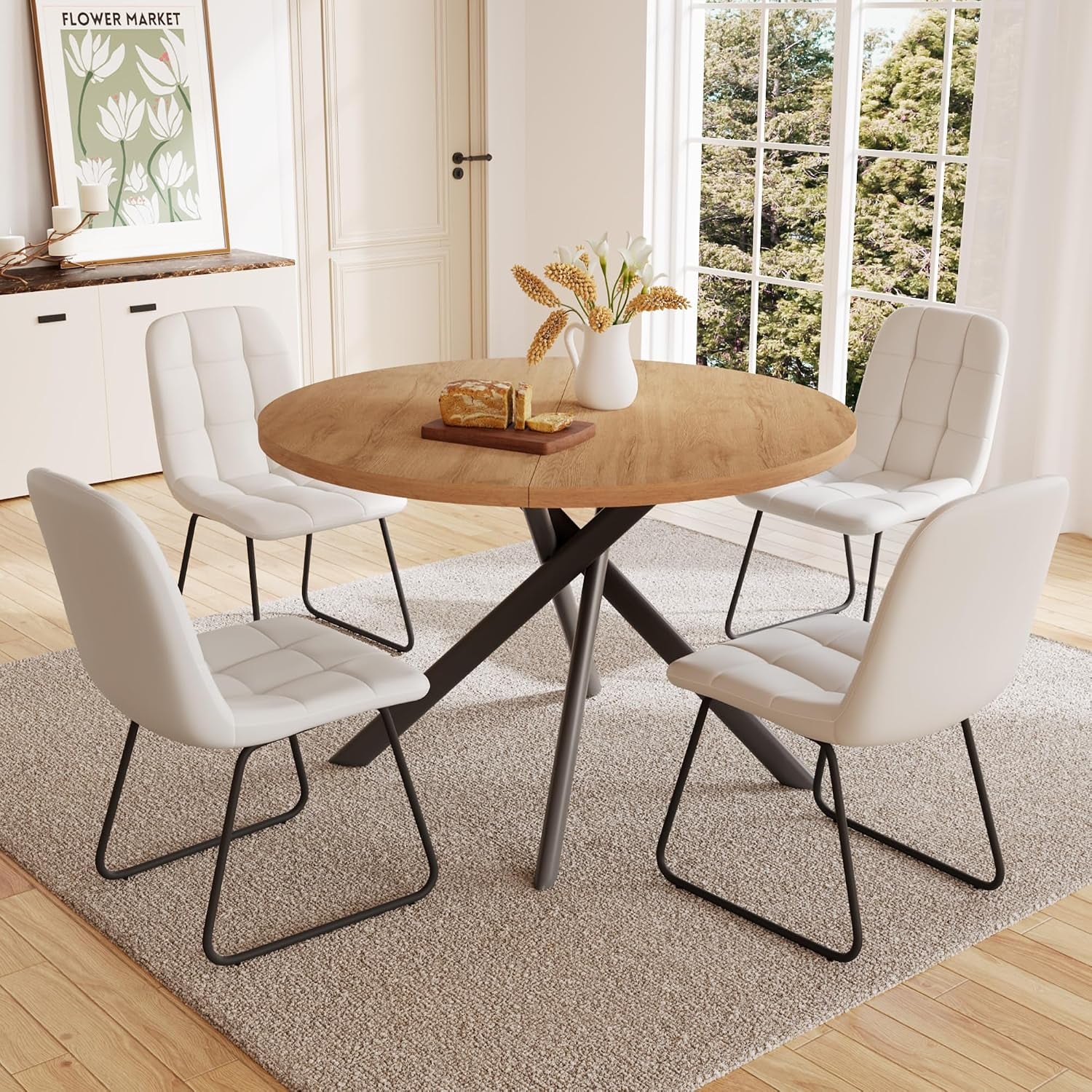 Round medium-brown wood table with dark crossed metal base and four white tufted chairs on sled frames.