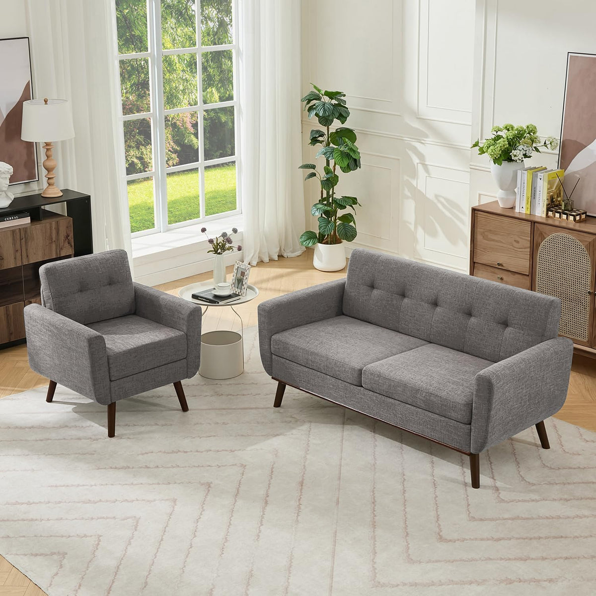 Angled view of a gray loveseat with tufted back next to a matching armchair and side table in a bright room