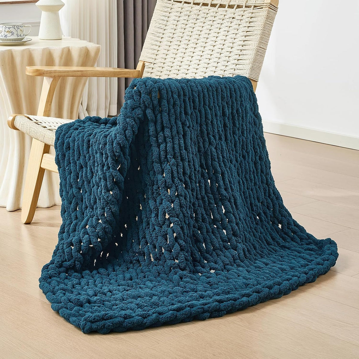 Dark teal chunky knit blanket casually draped over a woven lounge chair, pooling on the floor.
