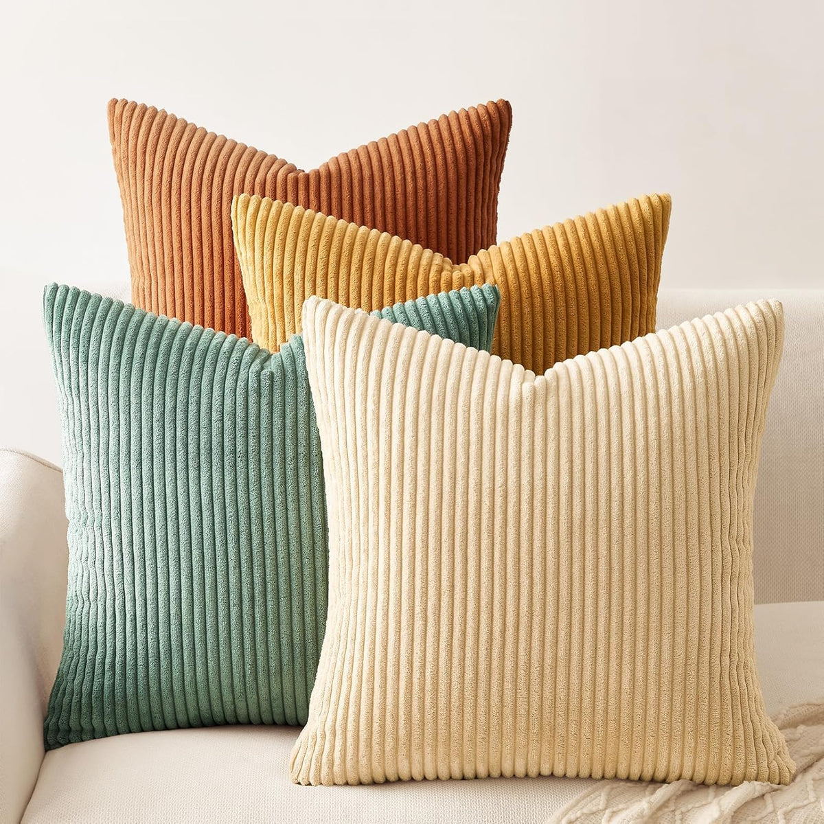 Four ribbed corduroy square pillows in burnt orange, mustard, teal and cream arranged on a sofa