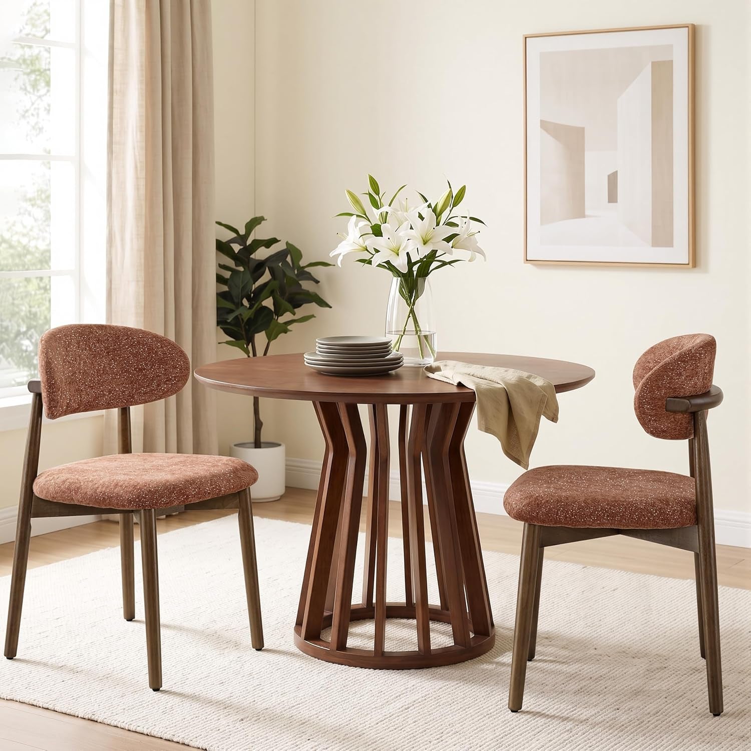 Two rust-brown upholstered chairs flank a round wood dining table in a neutral room.