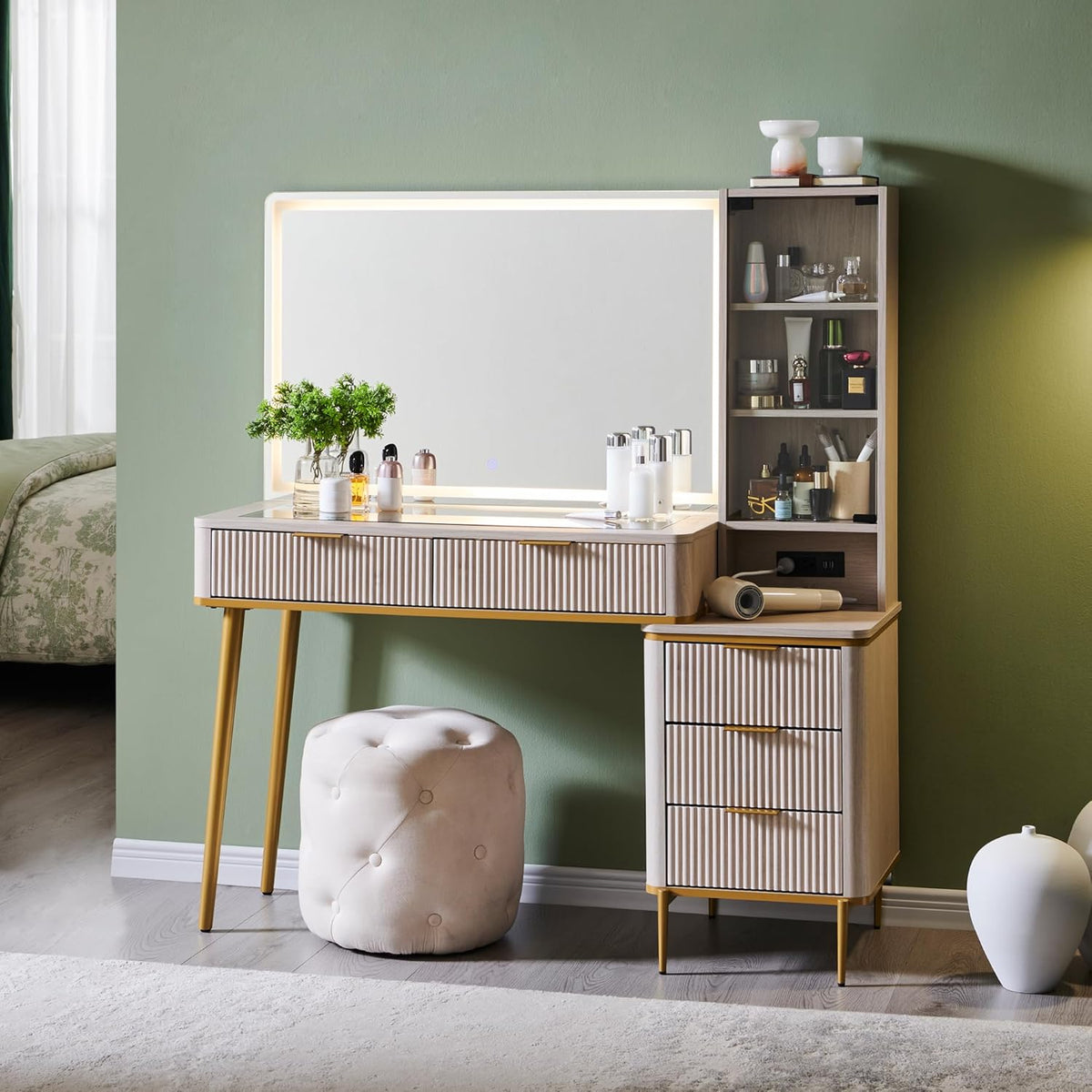 Full view of the lighted vanity set against a green wall with tufted round stool and decorative items on top.