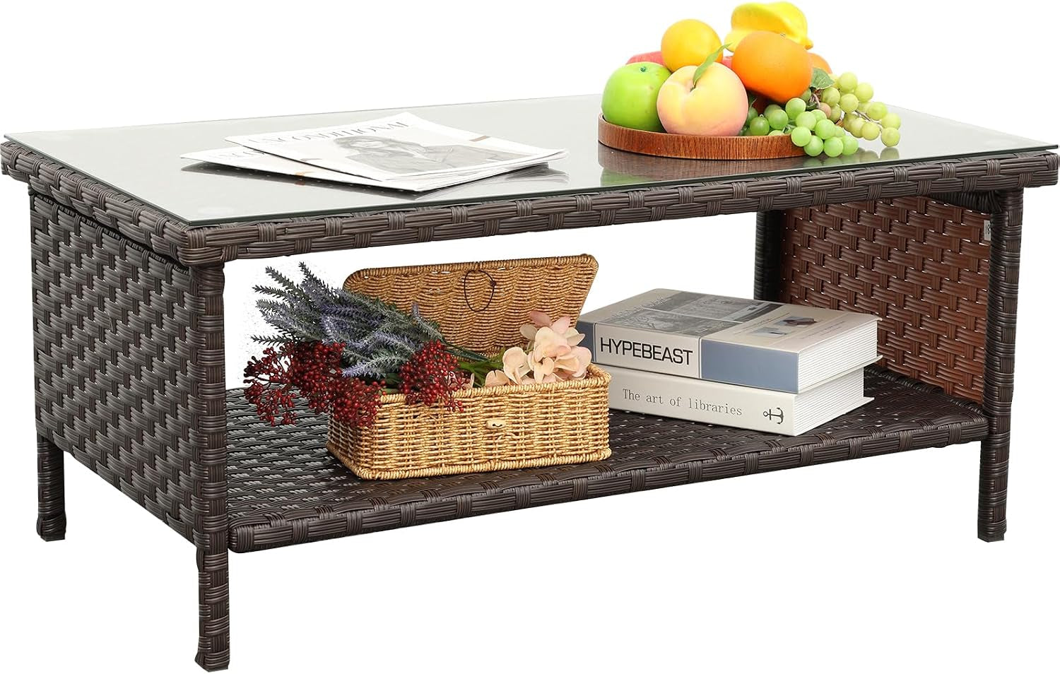Brown wicker outdoor coffee table on white background with fruit plate on top and a basket and books on the lower shelf