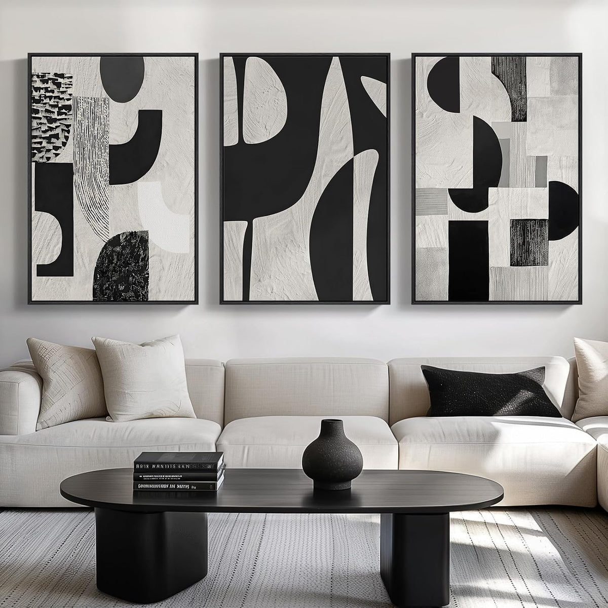 Three framed black-and-white abstract compositions with bold shapes above a neutral sofa and oval coffee table.