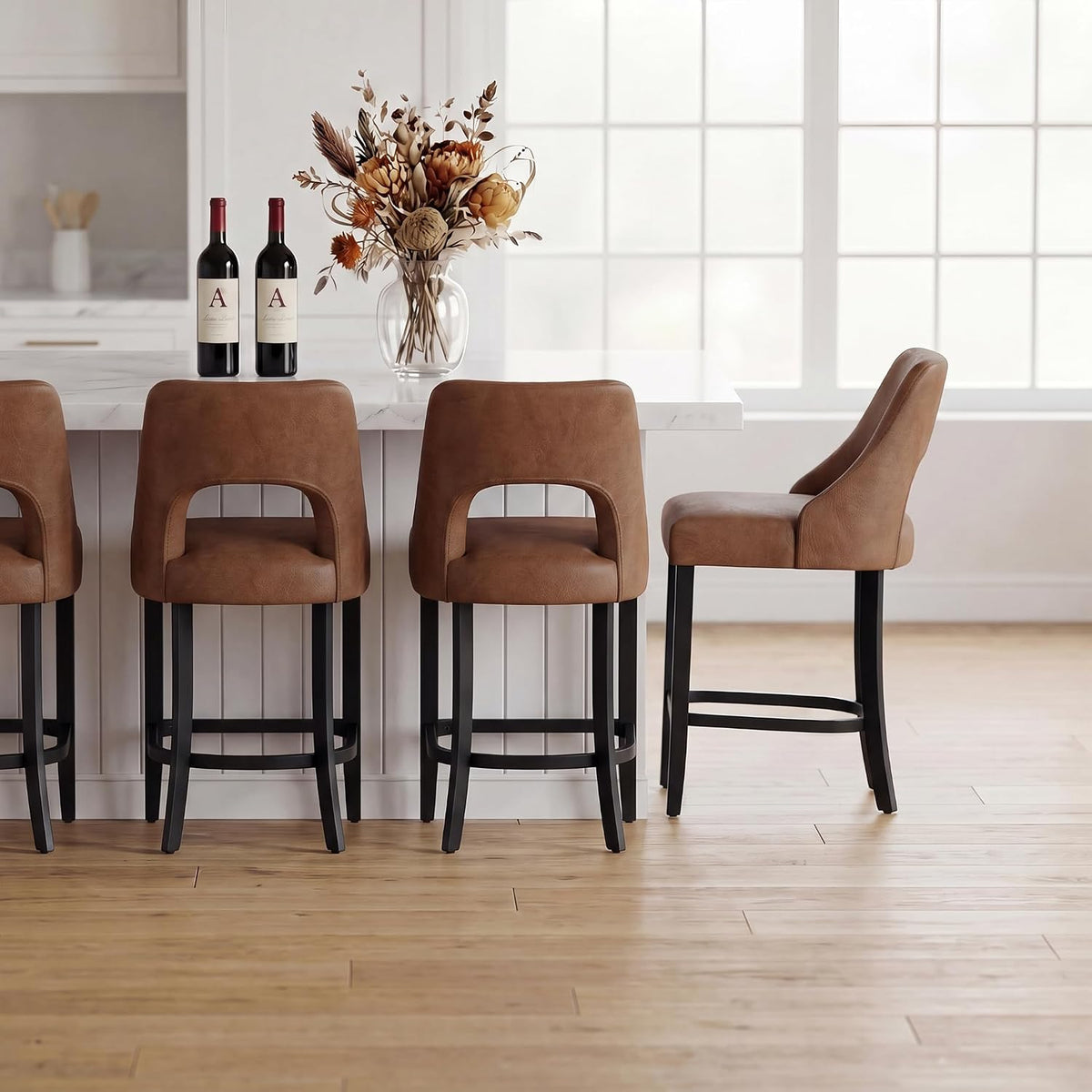 Three brown upholstered counter stools with black legs lined at a white kitchen island