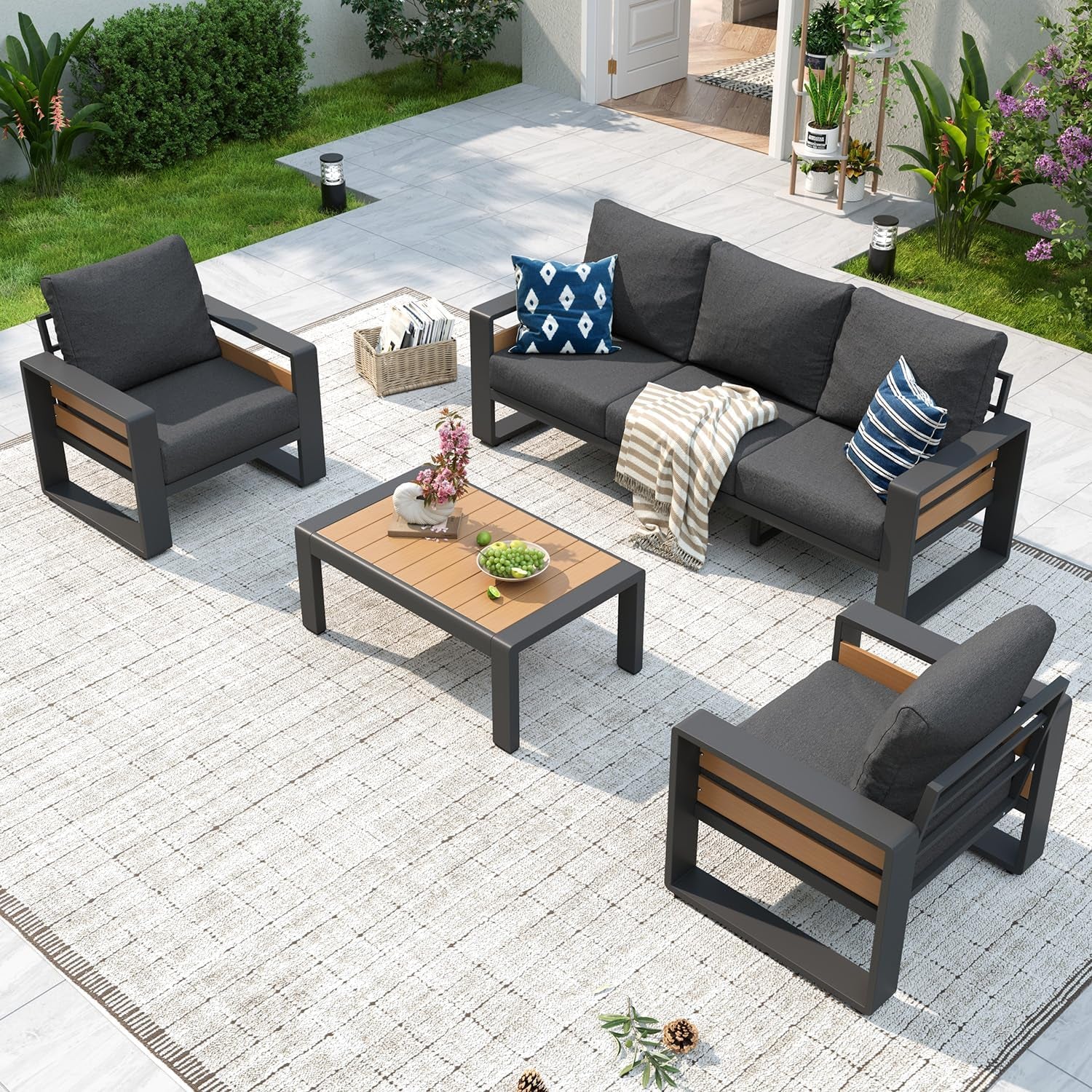 Outdoor sectional with charcoal cushions and dark frames surrounding a low wood-top coffee table on a neutral rug.