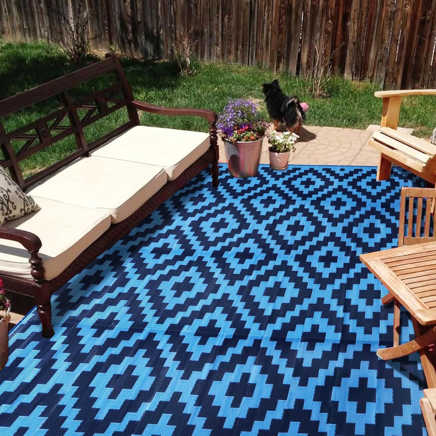 Large blue-and-black outdoor rug under patio seating with a small dog in background.