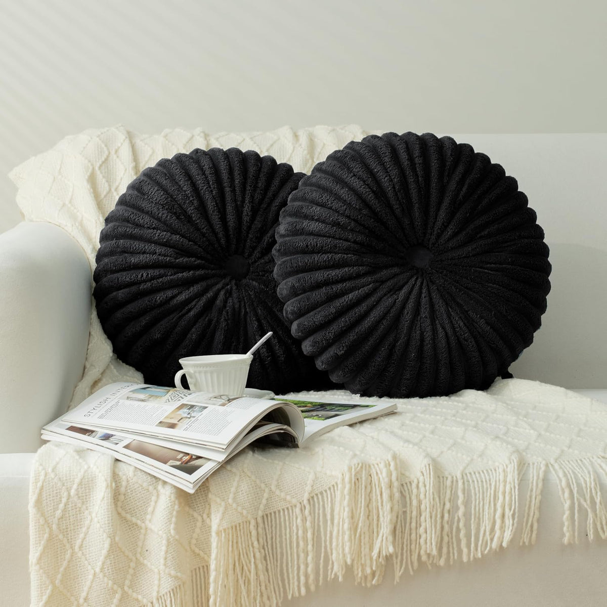 A pair of dark charcoal round ruched pillows with deep pleats on a textured throw.