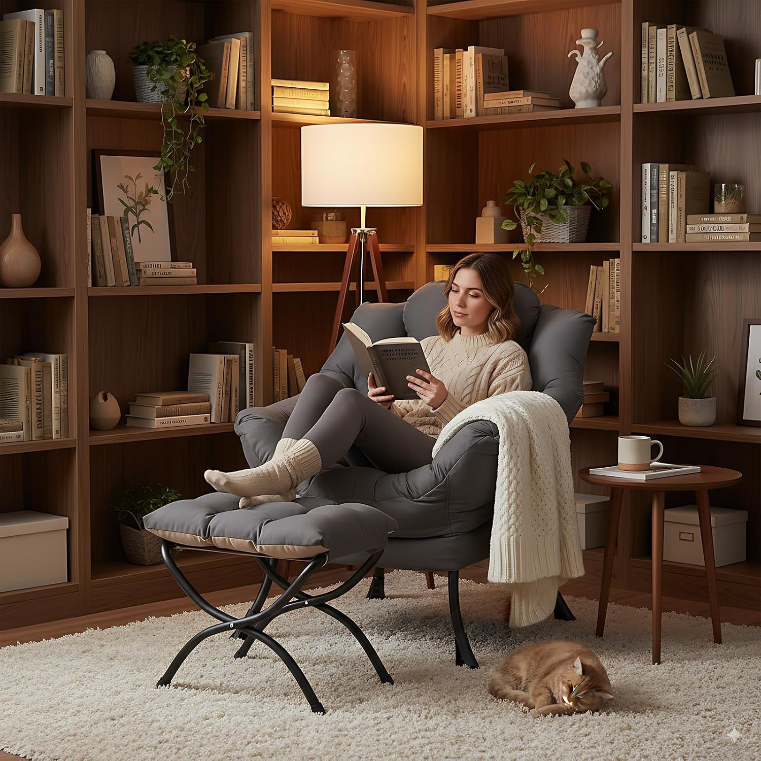 Woman reading in the grey padded chair with ottoman in a cozy library setting, a cat sleeps on the rug.