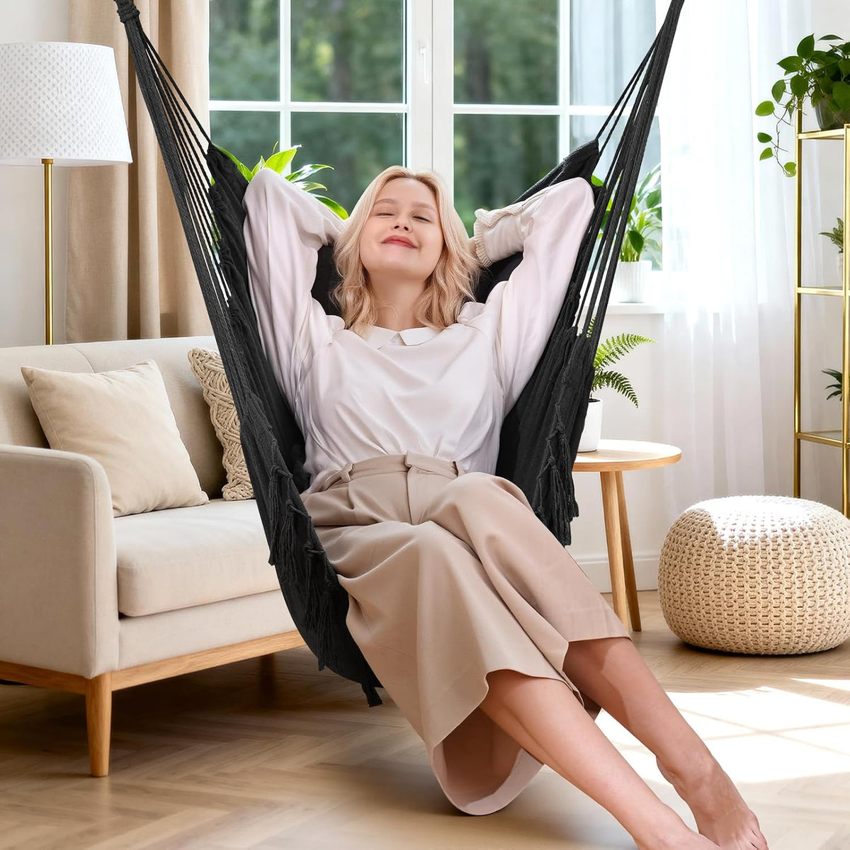 Dark grey hammock hanging chair in a bright living room with a woman reclining and relaxing in the seat