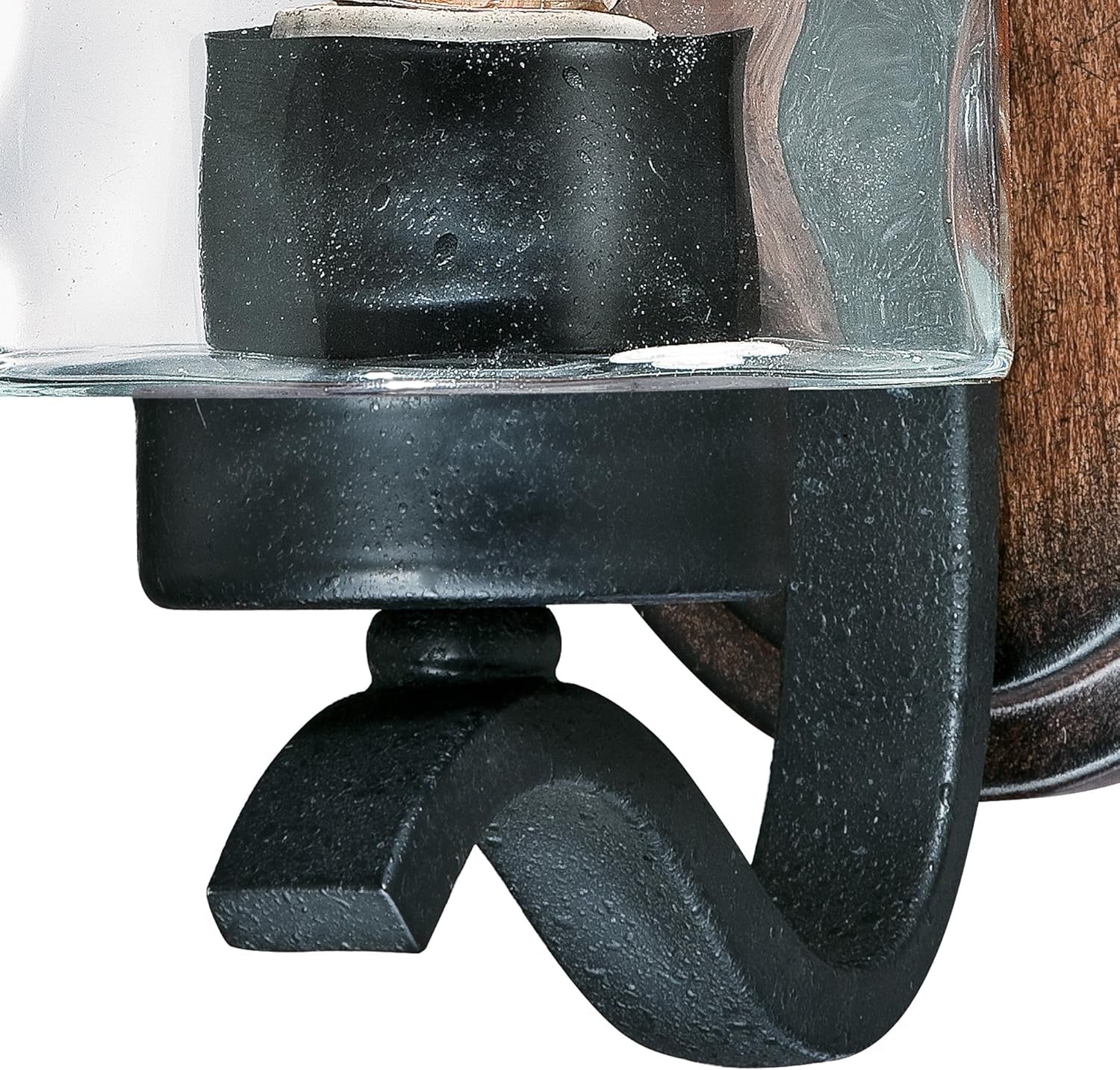 Close detail of textured black iron curved arm and the glass shade rim against the wood-tone back plate