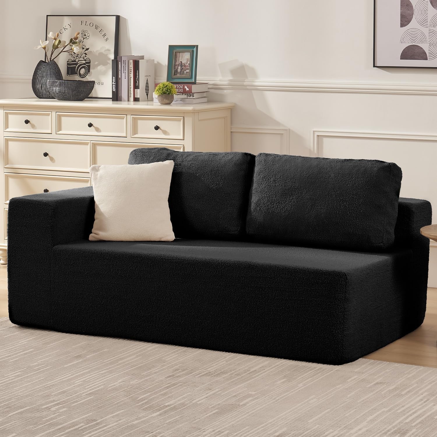 Black two-seat modular sofa with two back cushions and a cream throw and pillow in a styled living room.