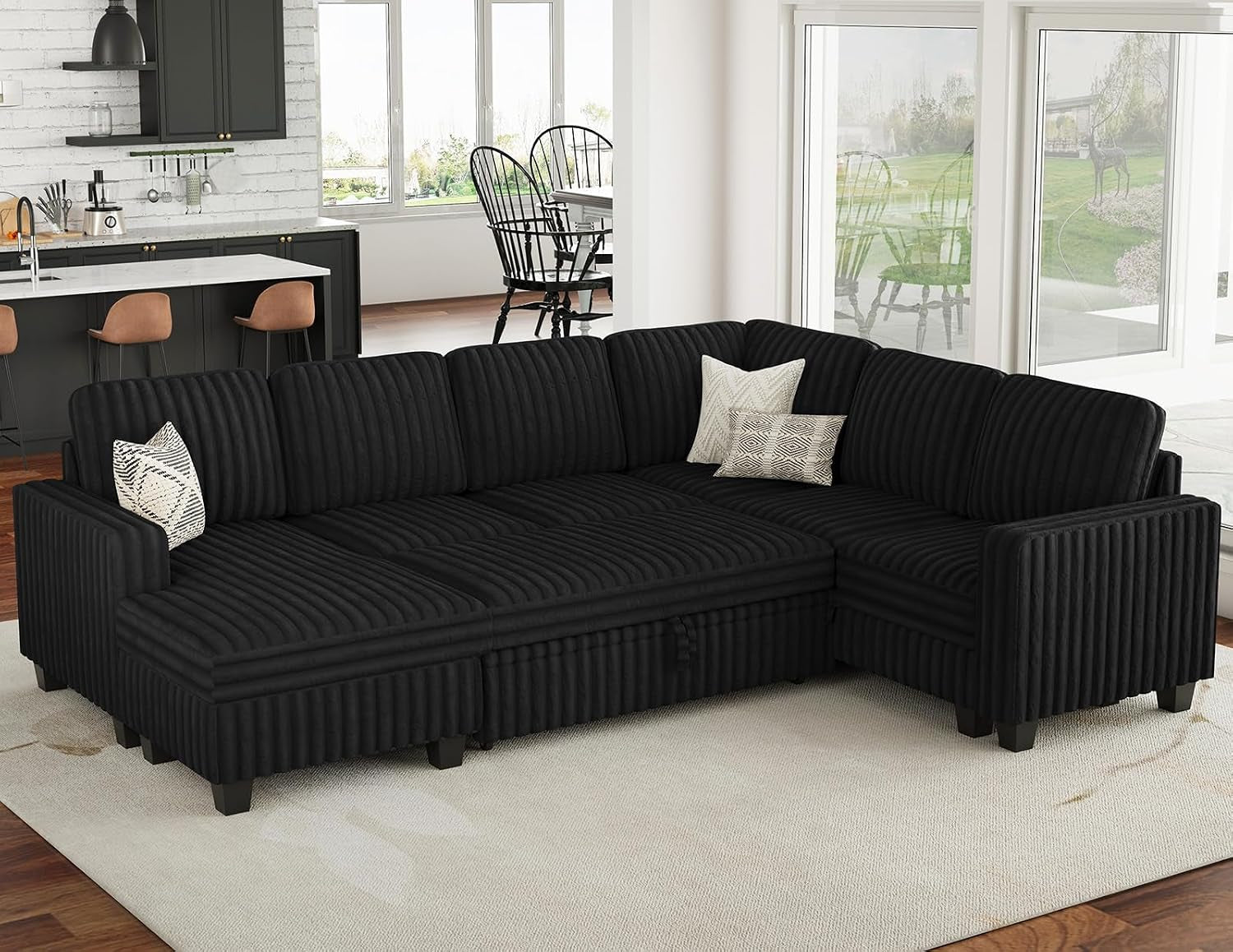 Black corduroy L-shaped sectional with two decorative pillows in an open-plan kitchen living area.