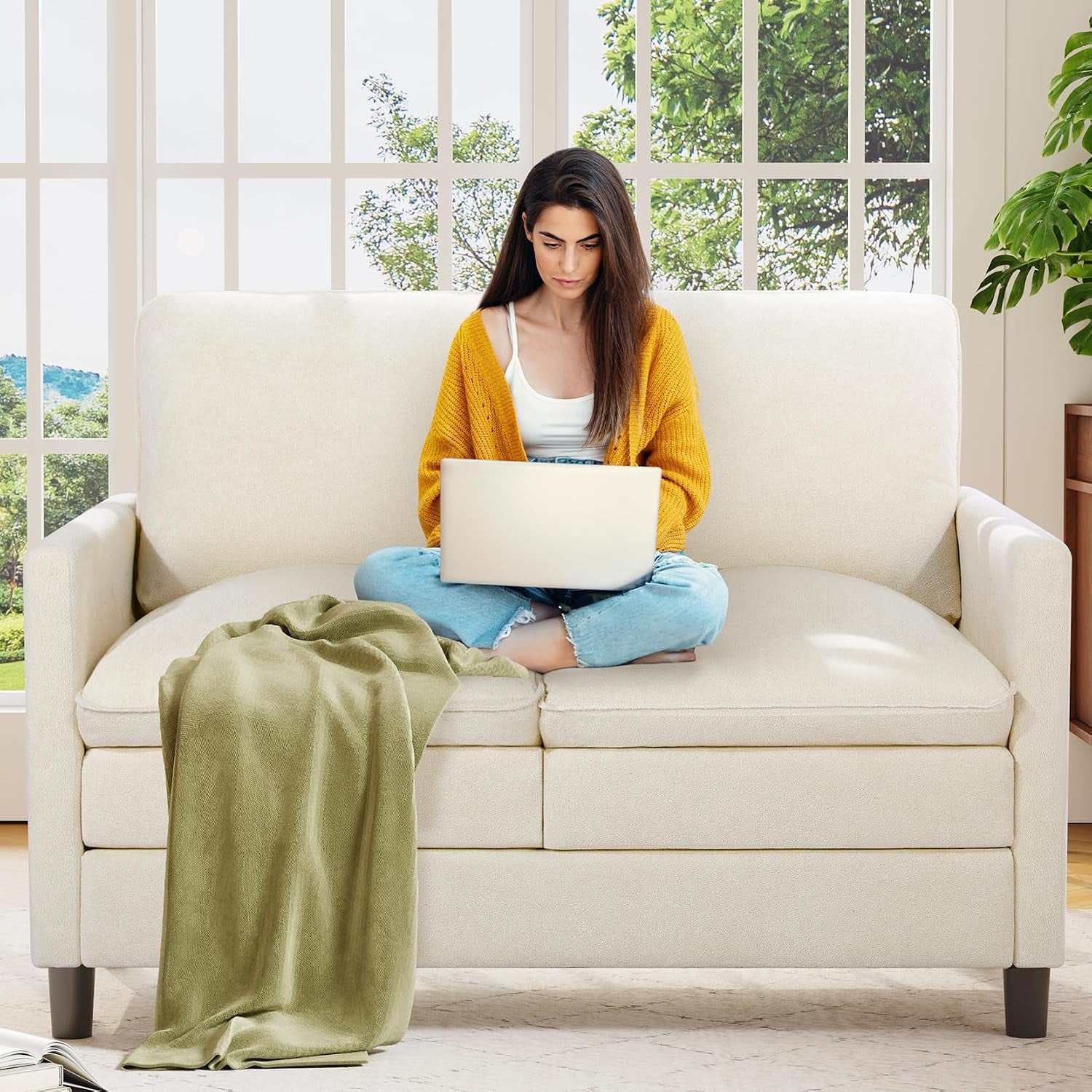 Light cream loveseat with a woman using a laptop and a green throw draped on the seat