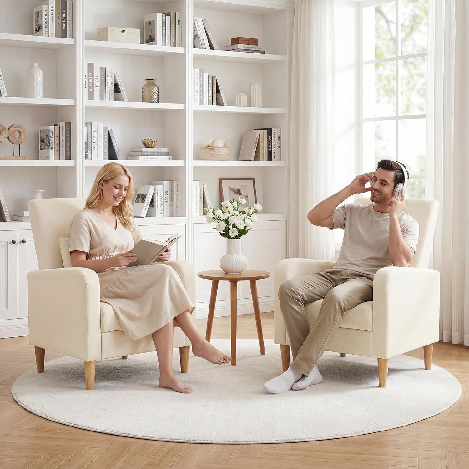 Two beige chairs in a bright living room setting with a man and woman seated to demonstrate scale