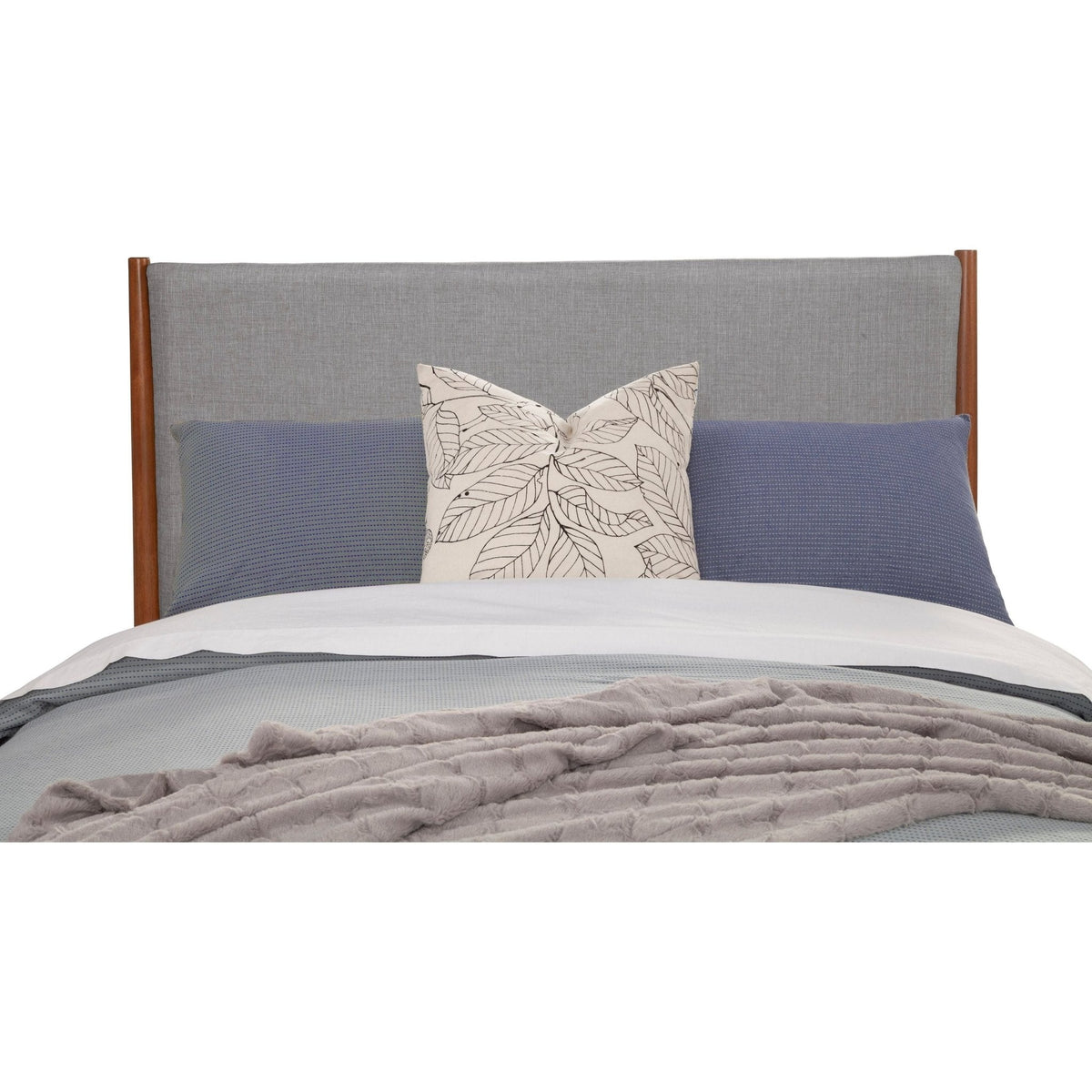 Gray upholstered headboard with warm wood posts above layered pillows and a rumpled blanket.