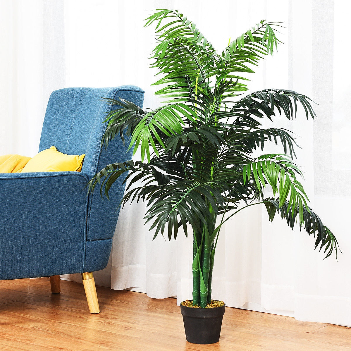Artificial palm in a black pot beside a blue armchair with a yellow cushion.
