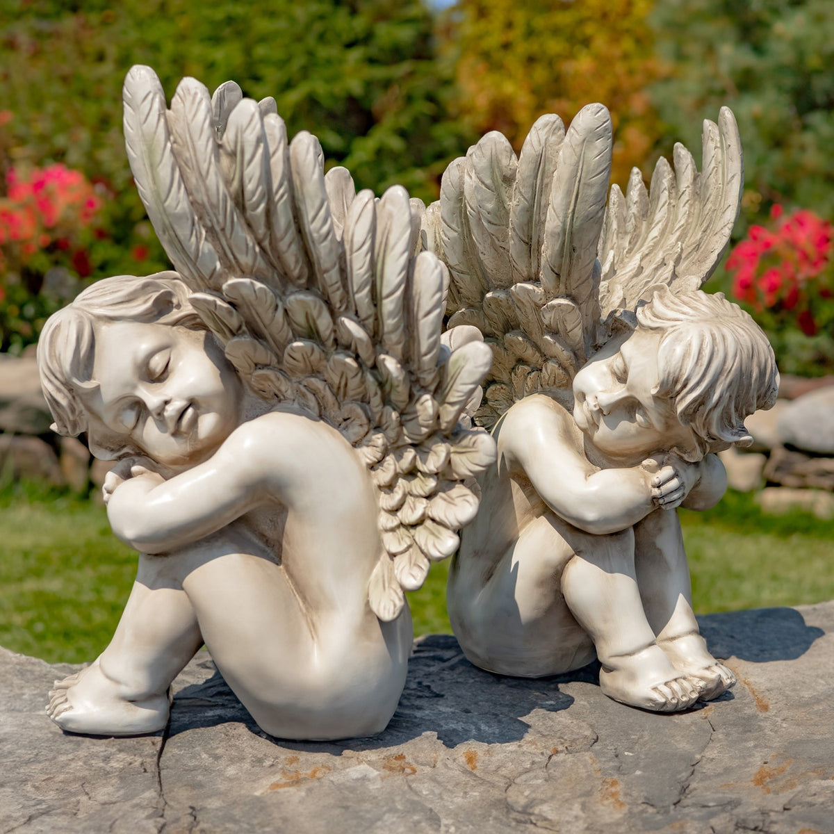 Pair of antique grey sitting cherub statues on a garden stone ledge