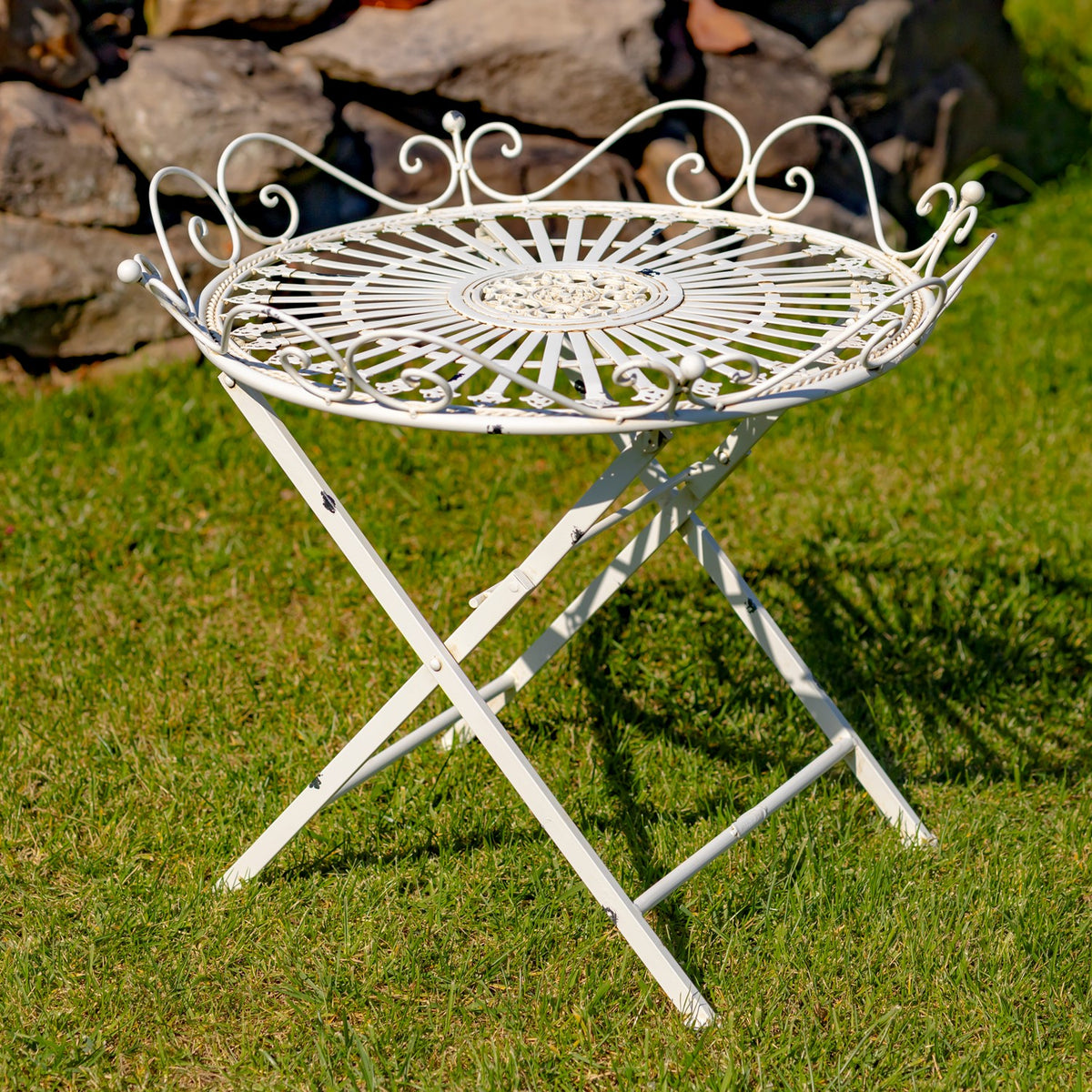 White round folding iron table with a radial openwork top and curled rim, standing on grass.