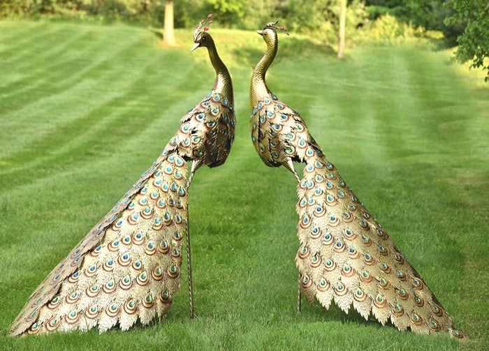 Pair of gold peacock sculptures with jeweled tails standing on a green lawn