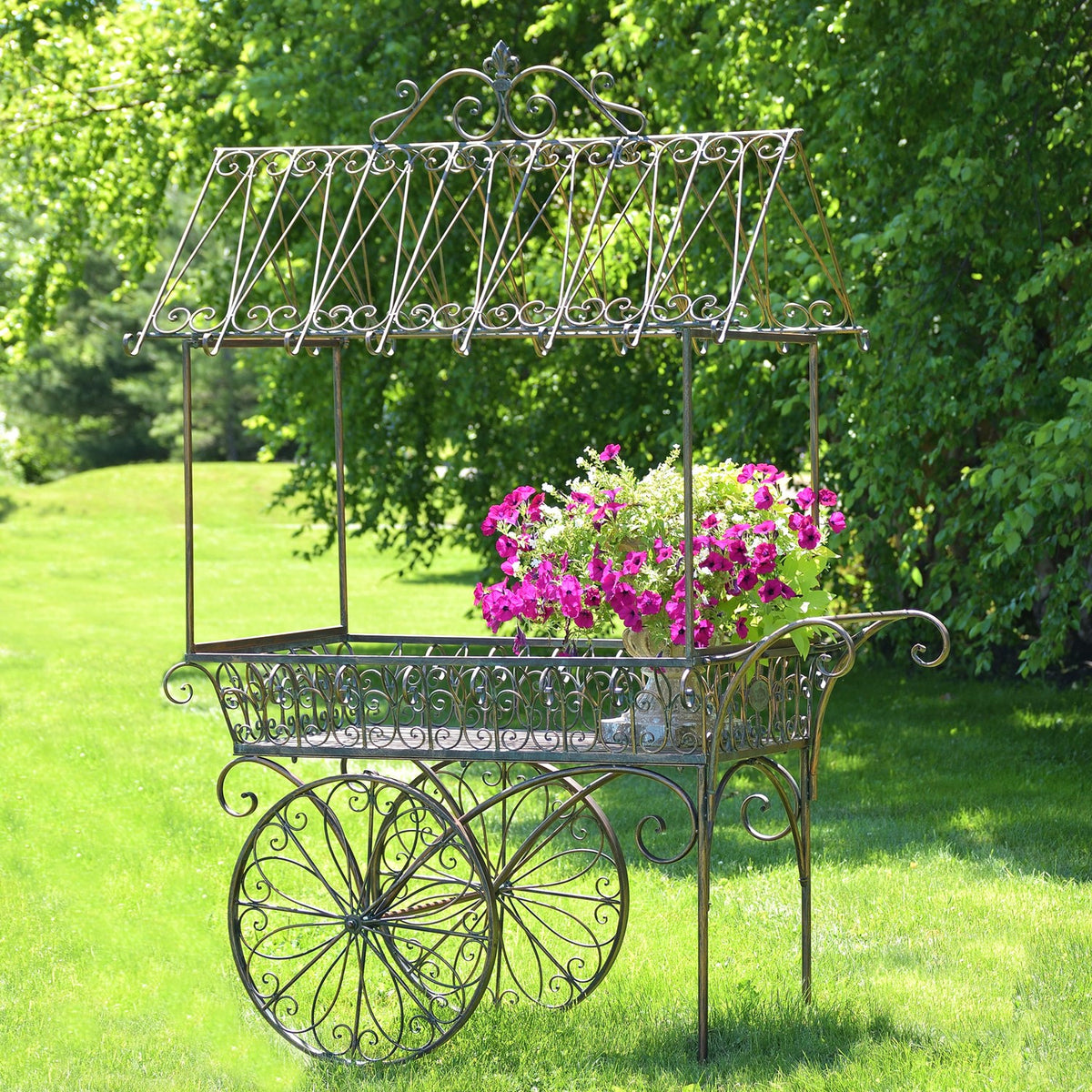 Ornate iron flower cart with magenta blooms on a lawn, shown with its tall decorative canopy.