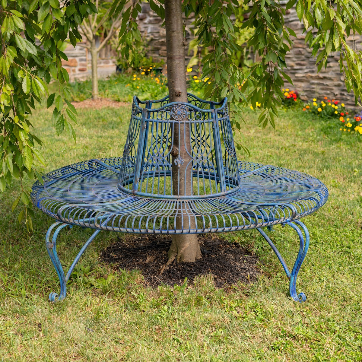 Blue circular metal bench encircles a tree, with curved legs on a lawn.