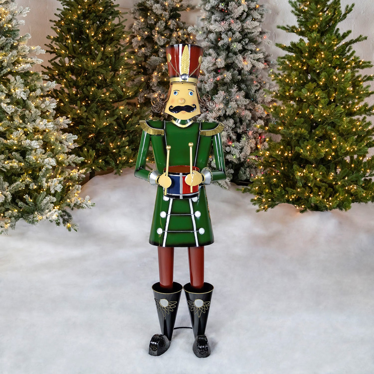 Full green nutcracker holding a drum in front of decorated Christmas trees
