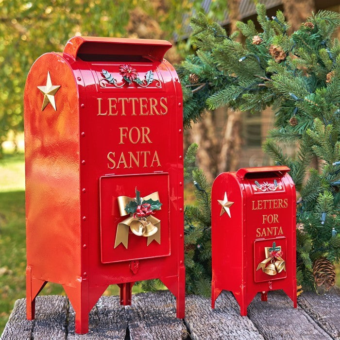 Two glossy red Santa mailboxes with gold details on a garden path beside evergreen branches