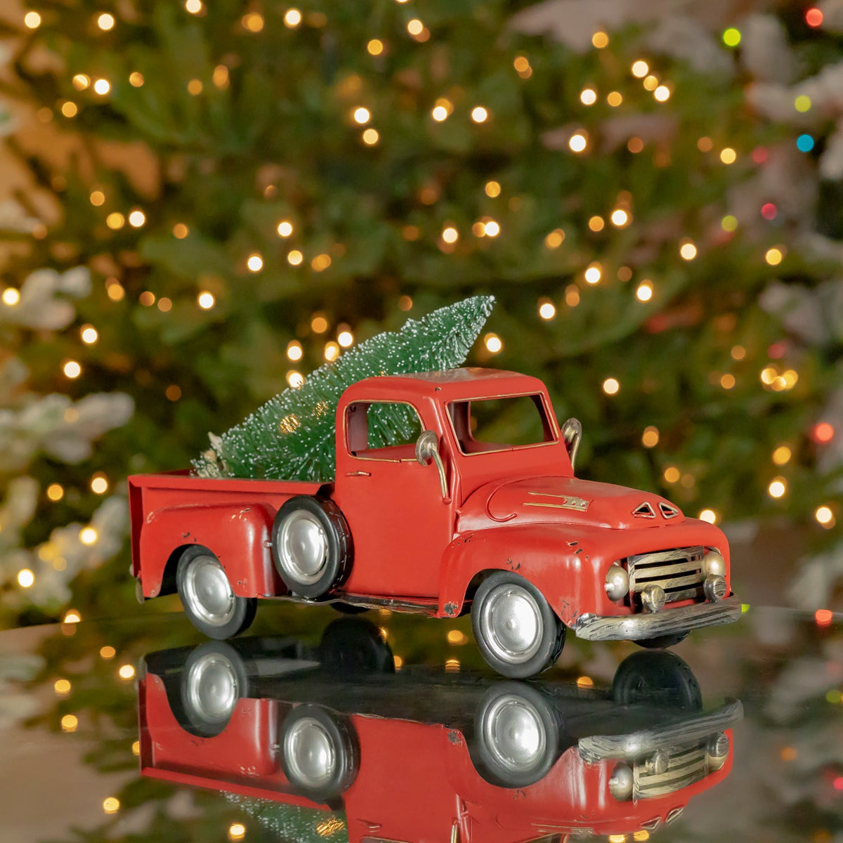 Distressed red pickup carrying a green Christmas tree, shown against a glowing holiday tree.