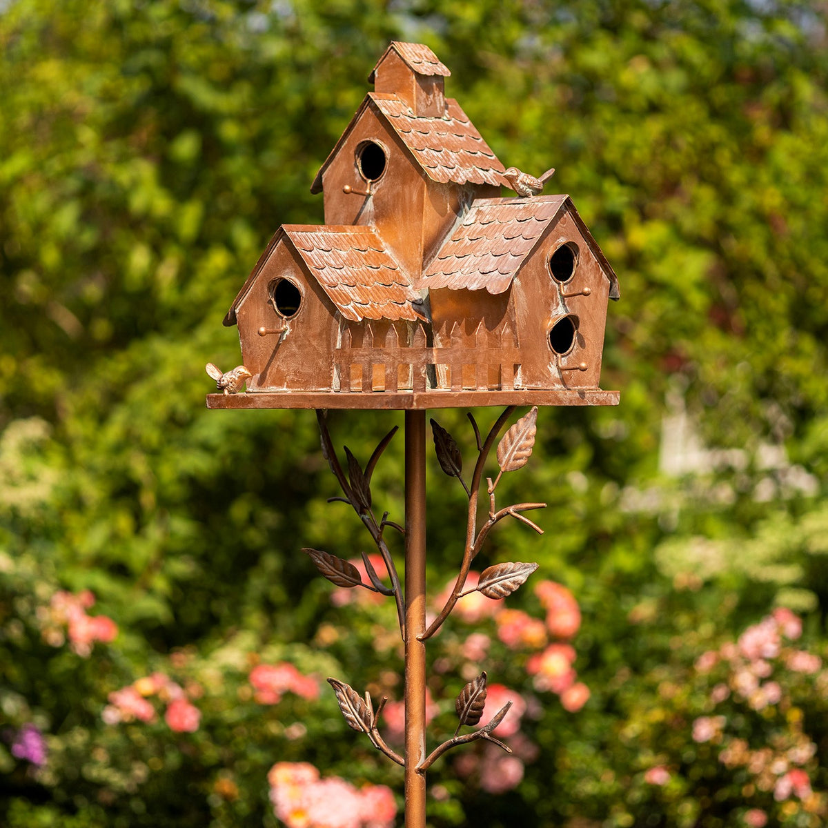Antique copper-toned birdhouse cluster on a decorative stake, front view among flowers
