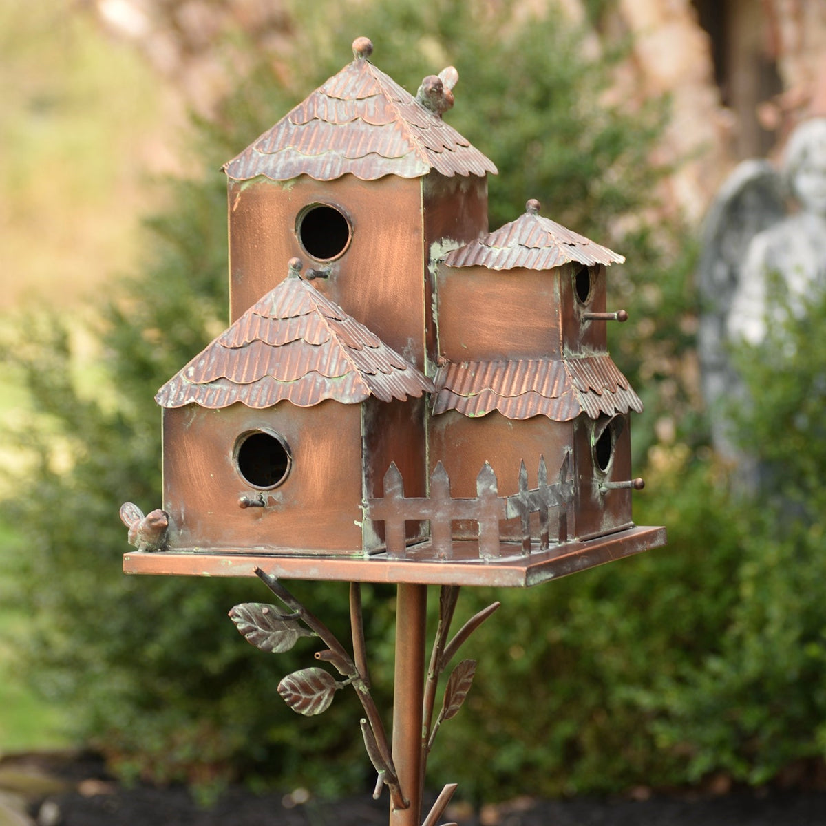 Close view of a rust-toned metal birdhouse cluster with layered roofs, round openings and small bird accents.