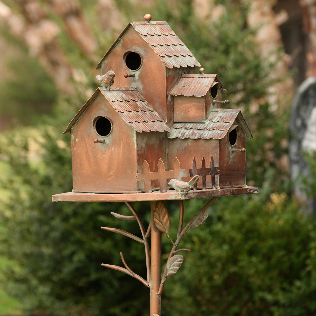 Antique copper birdhouse stake viewed from the front among green garden foliage