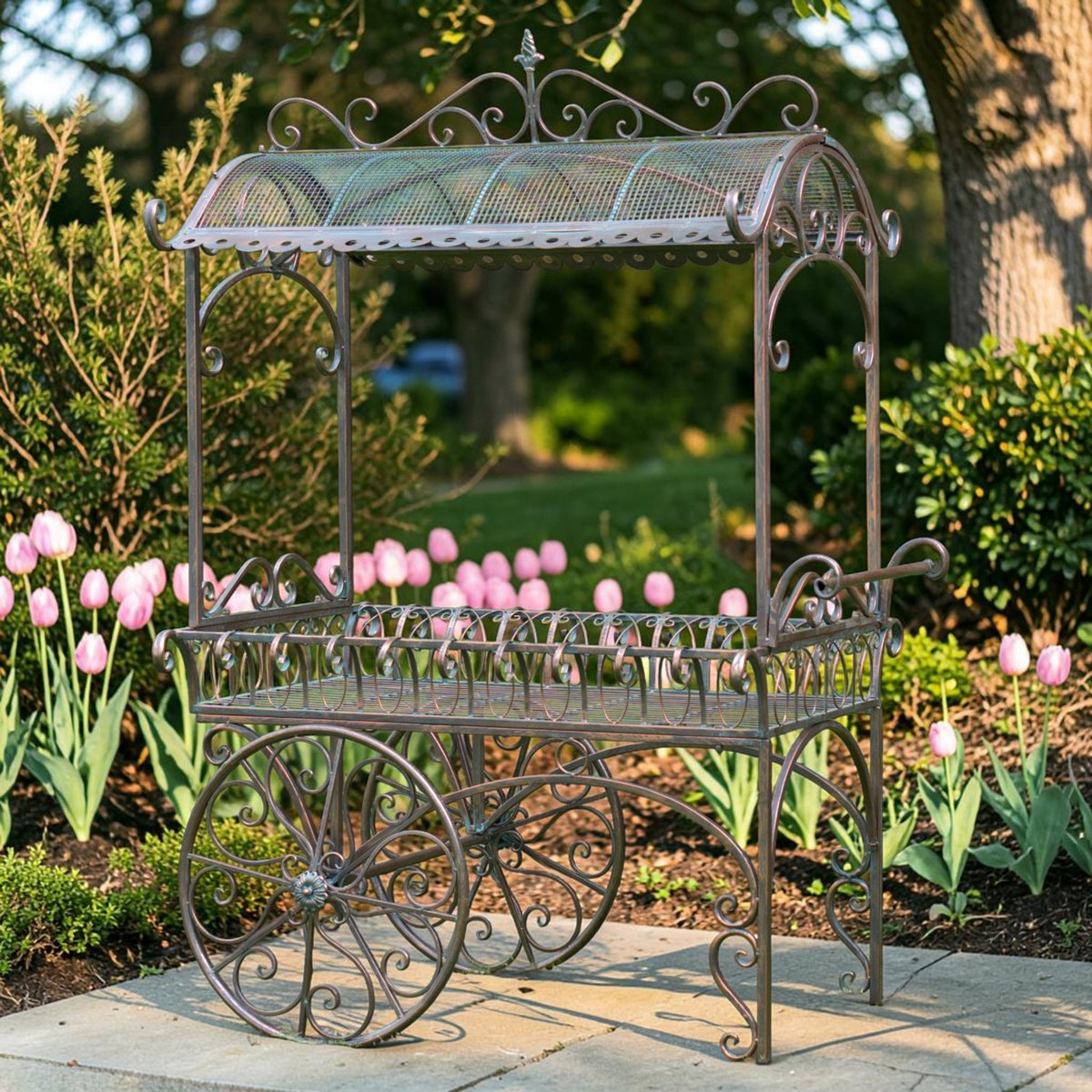 Ornate iron flower cart with a curved mesh roof stands among pink tulips on a stone path.