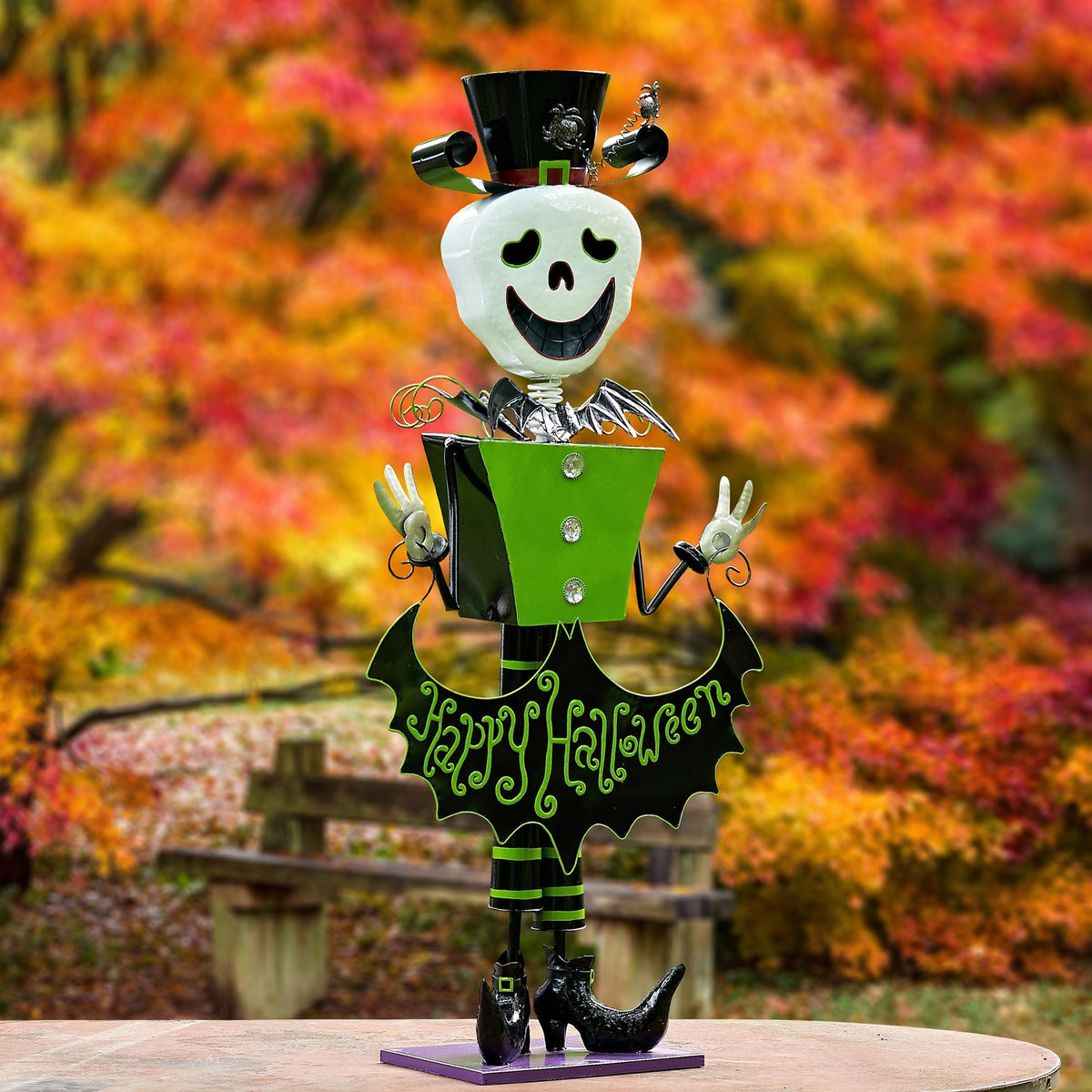Full view of a smiling skeleton figurine in a green coat and top hat, standing on a purple base outdoors.