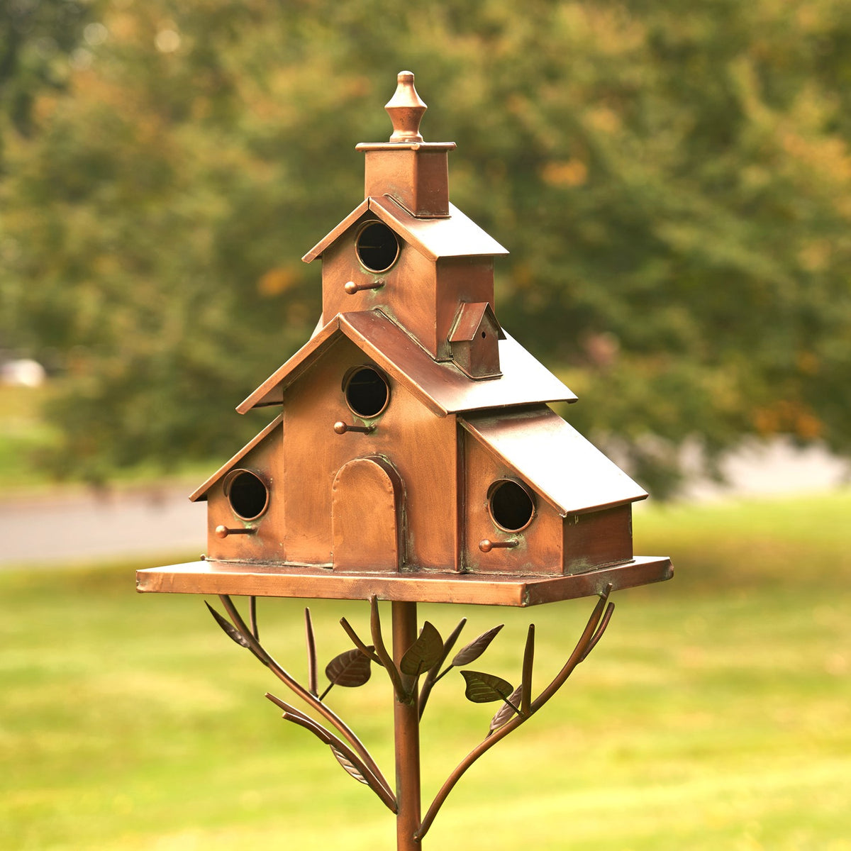 Front view of a copper-colored tiered birdhouse with round openings and a decorative branch-like stake.