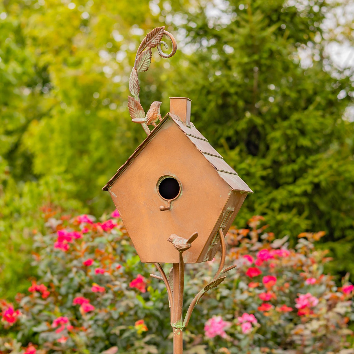 Antique copper birdhouse stake close-up among colorful garden flowers